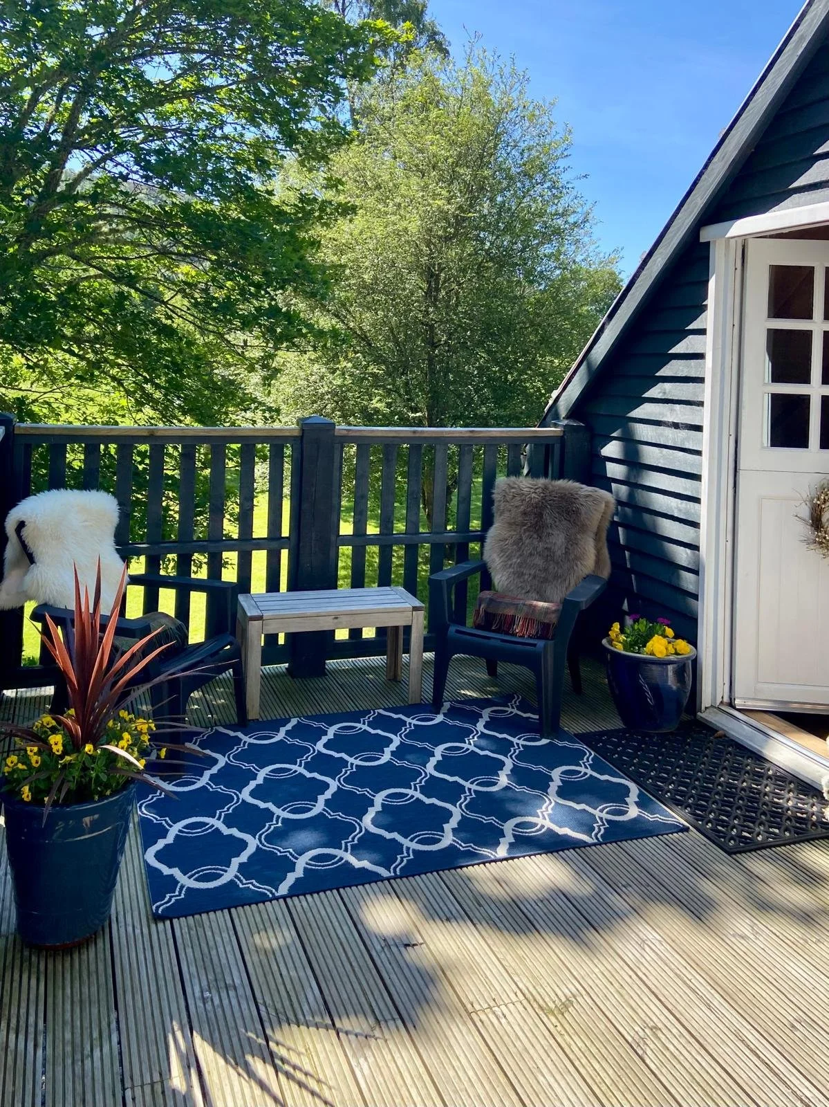 Private deck at The Hayloft with outdoor seating and rug, surrounded by green woodland.