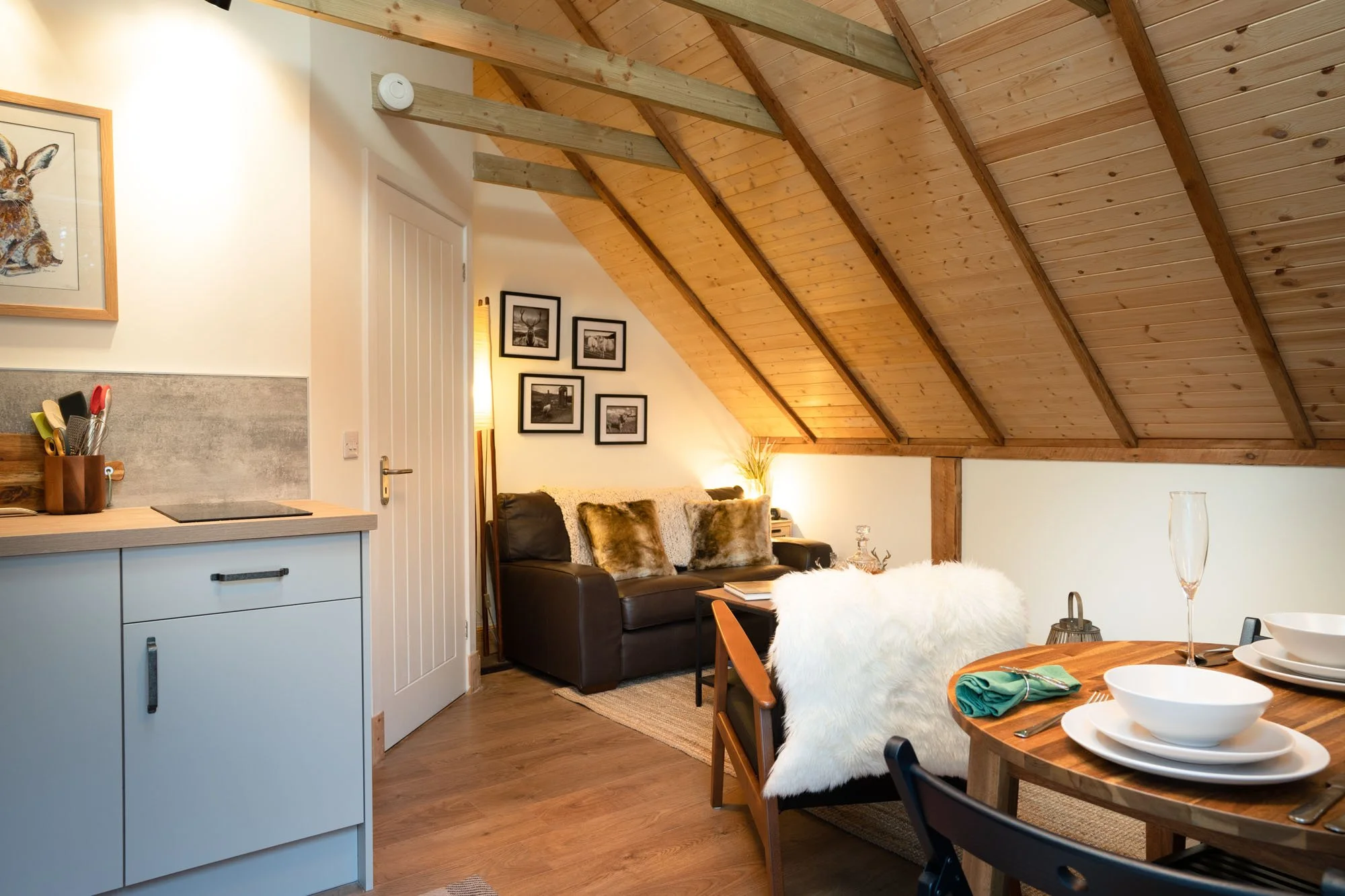 Open-plan kitchen, dining and living space at The Hayloft, with timber vaulted ceiling and warm wooden flooring.