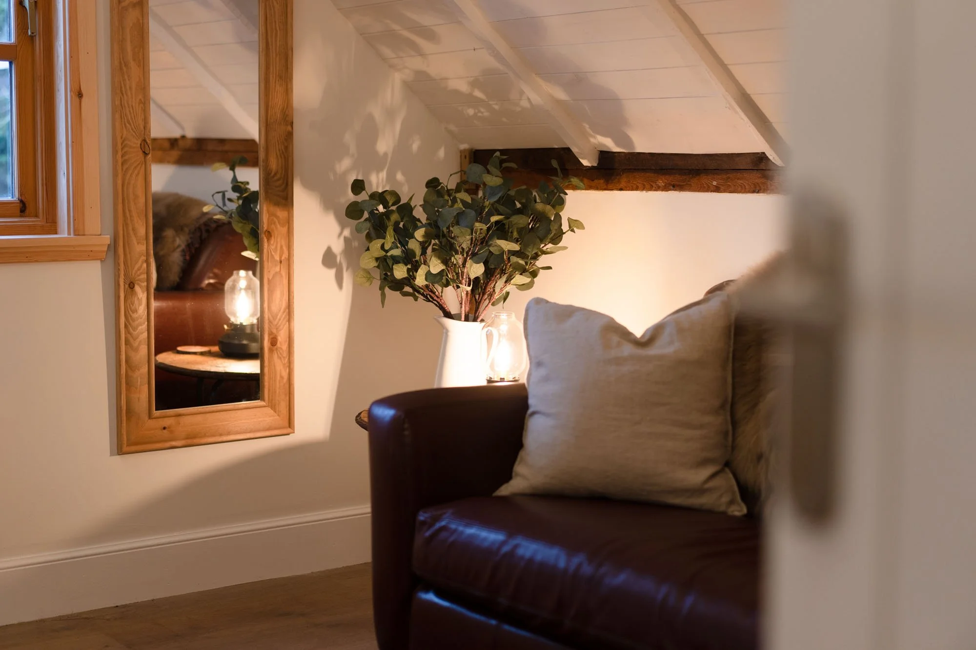 Leather sofa, cushions and foliage beneath the sloping ceiling in The Hayloft bedroom.