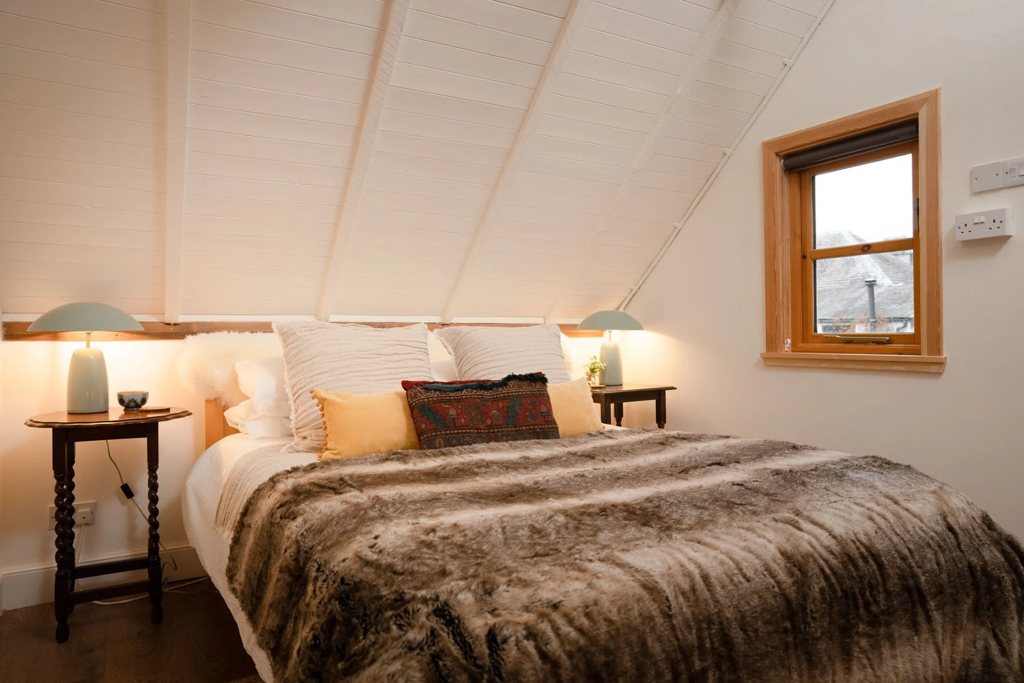 Double bedroom at The Hayloft with faux-fur bedspread, bedside lighting and woodland view from the window.