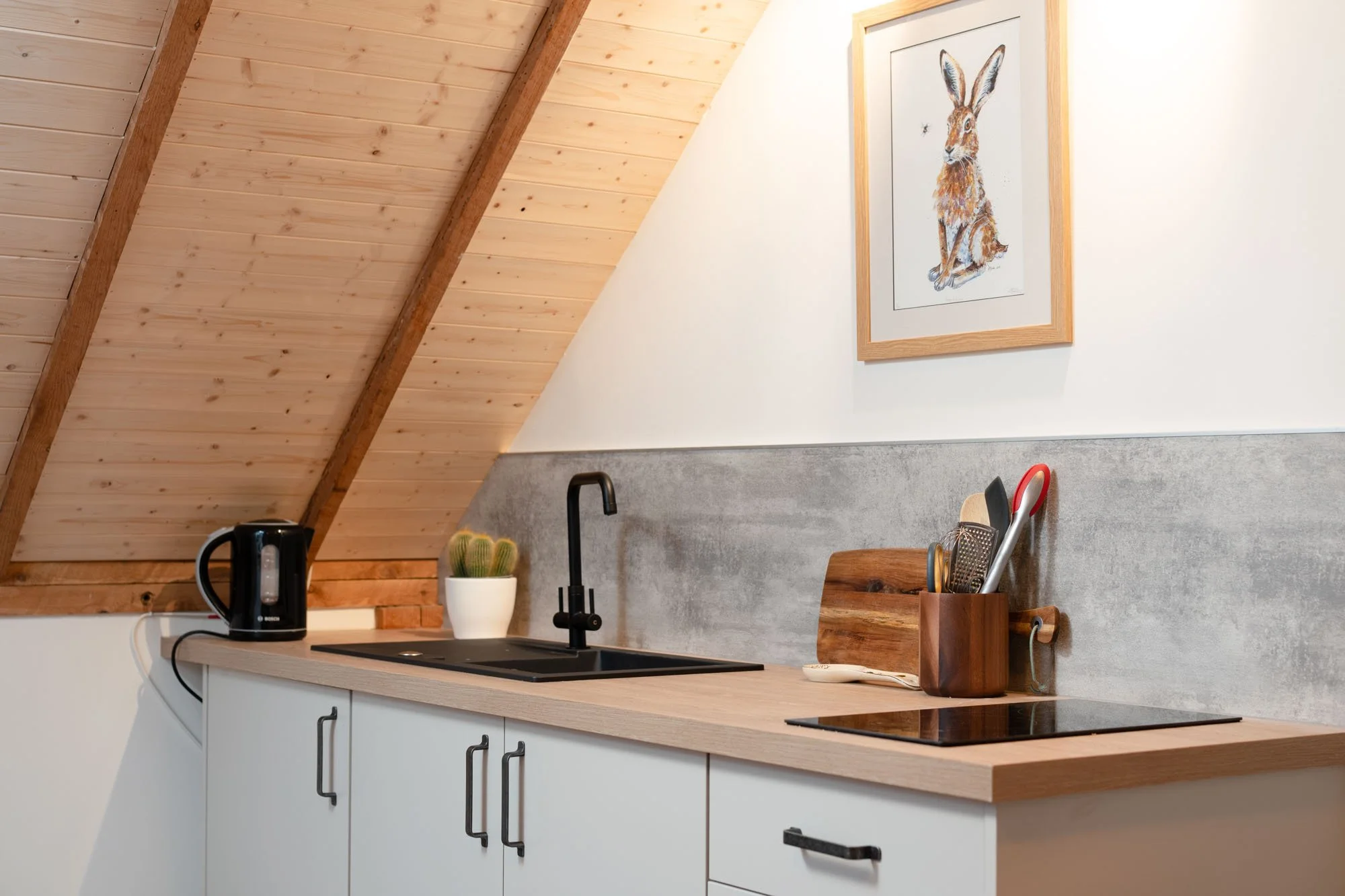 Compact modern kitchen at The Hayloft with wooden worktop, black tap and timber-clad vaulted ceiling.