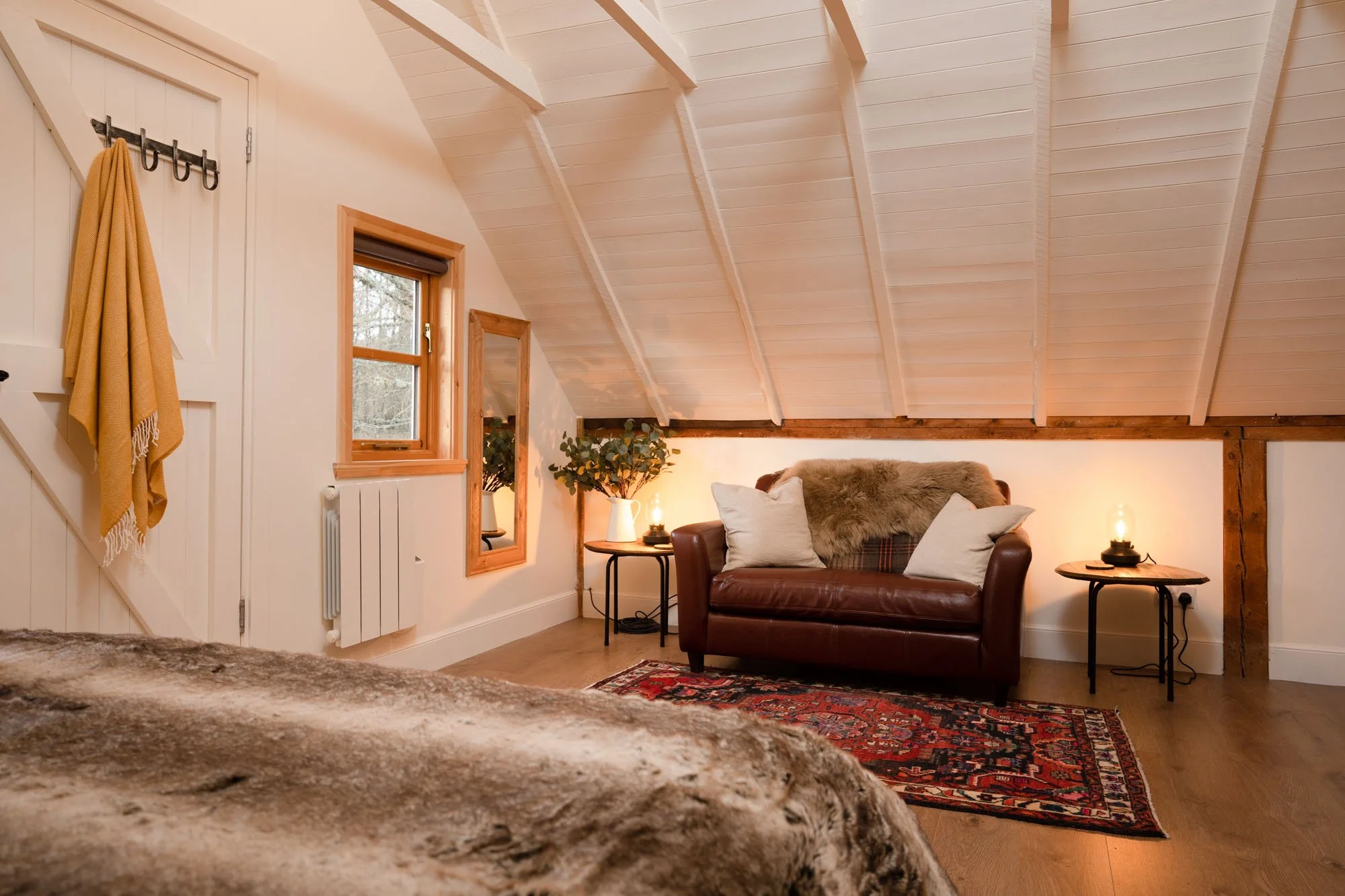 Cosy bedroom seating area at The Hayloft with leather sofa, patterned rug and warm bedside lighting.