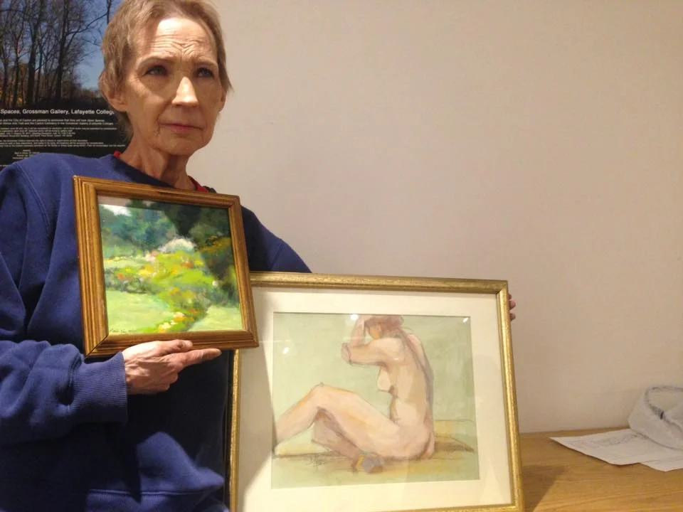 Patti holding two donated paintings: "A Pocketful of Roses" oil on board by Li-hsien Price $200 and also a figure painting by Donna Needs (sold). 