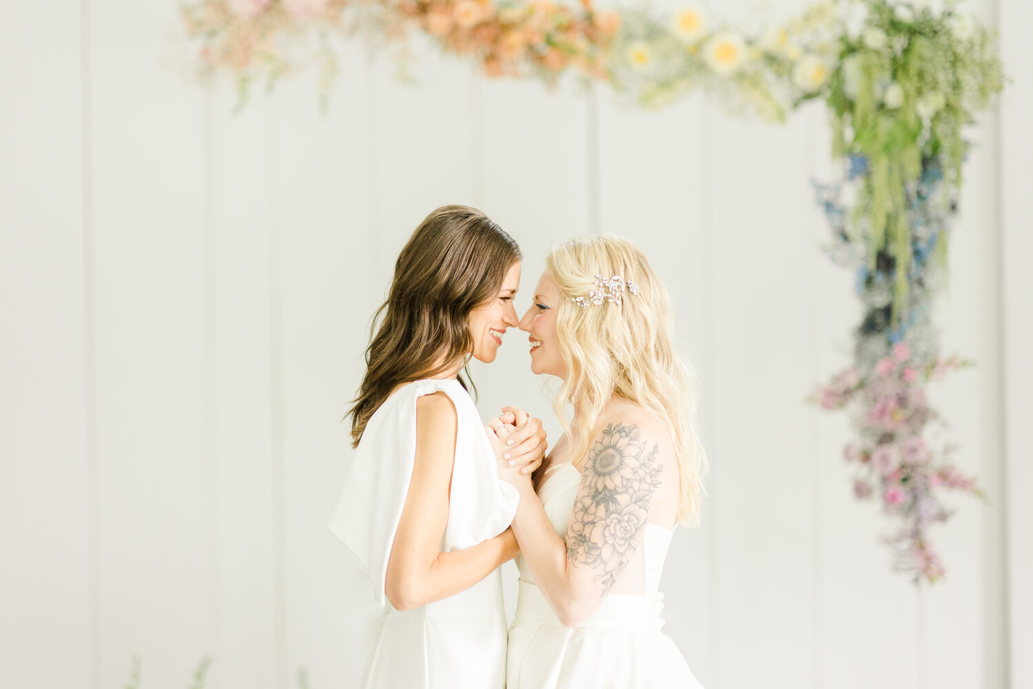 Brides holding hands wearing Windham jumpsuit and Ines Di Santo Quice wedding dress.