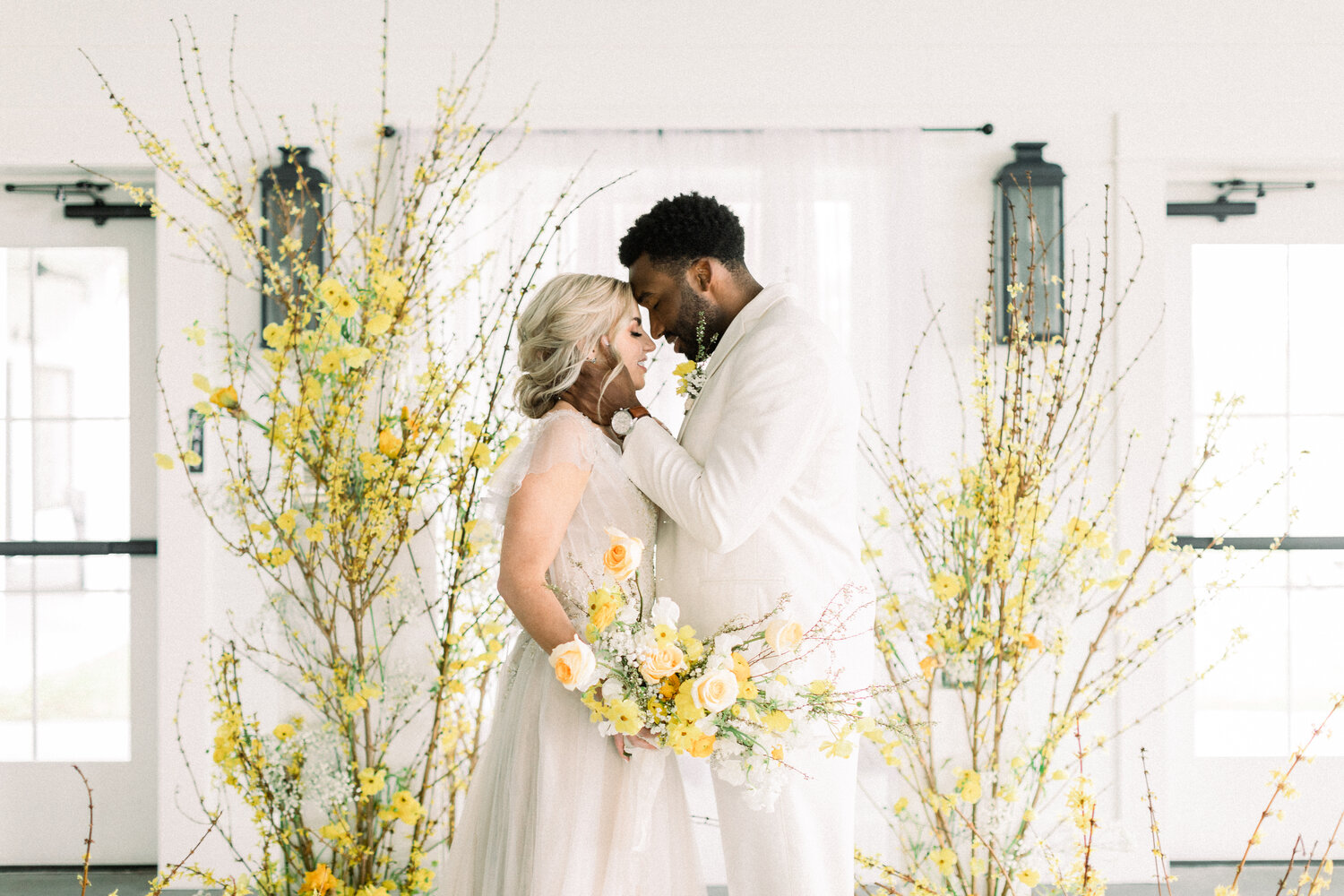 Bride and groom posing for wedding ceremony photos with yellow and white florals.
