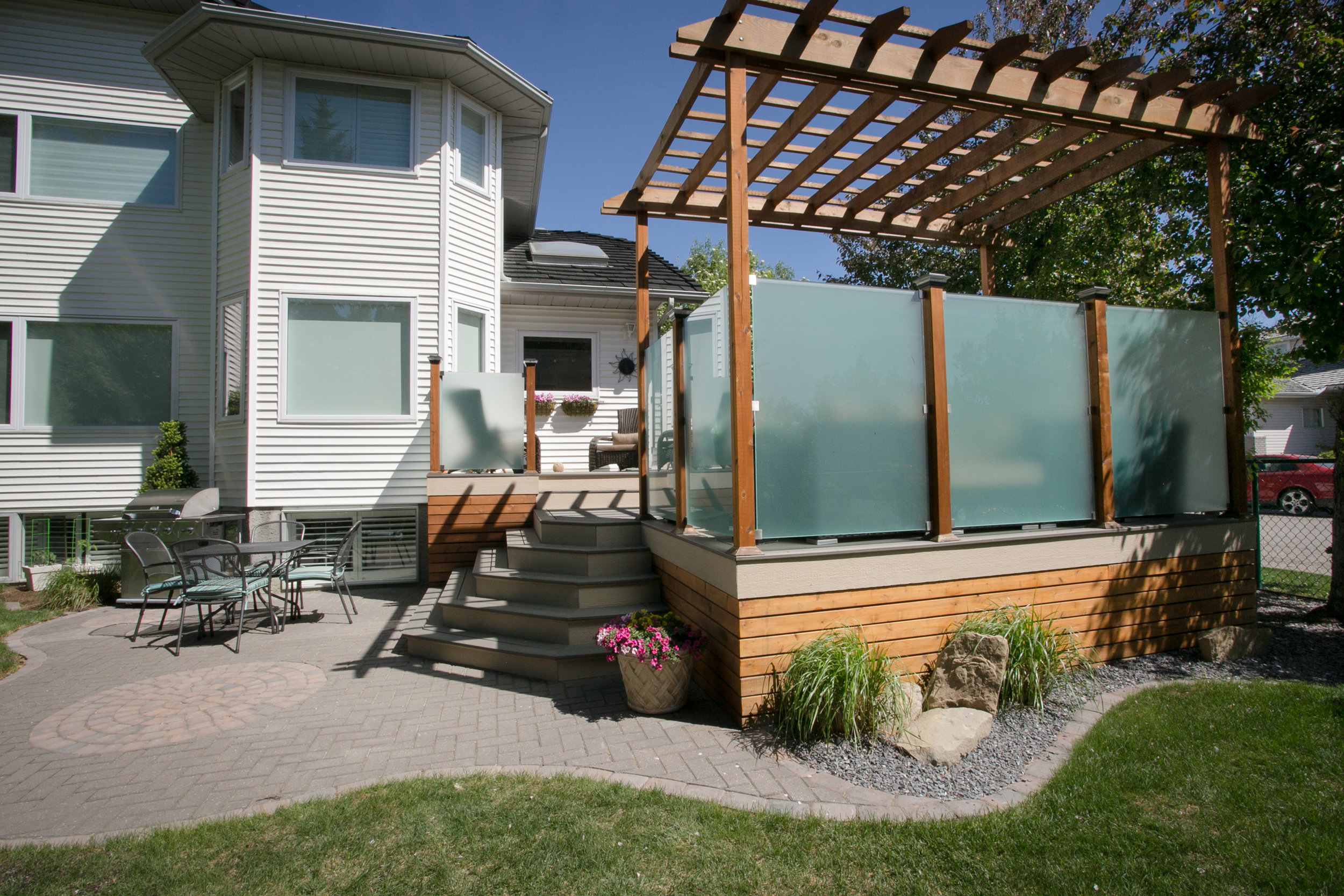  Shaped paving stone patio, plant beds, custom deck with privacy panels and pergola — Valley Ridge, Calgary. 