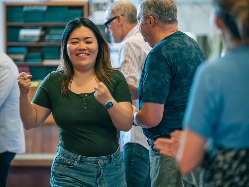 A young woman smiling and dancing among a group of people in an indoor setting.