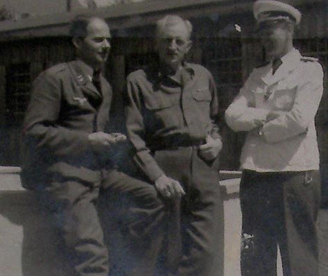 Scharff is on the left, an American POW is in the middle, and a Luftwaffe officer on the right. "YOU SHALL TELL US WHAT WE WISH TO KNOW, OR HERR OFFICER AND I SHALL HAVE TO... uh... make a note of that and send you back with some coffee to share with the others."