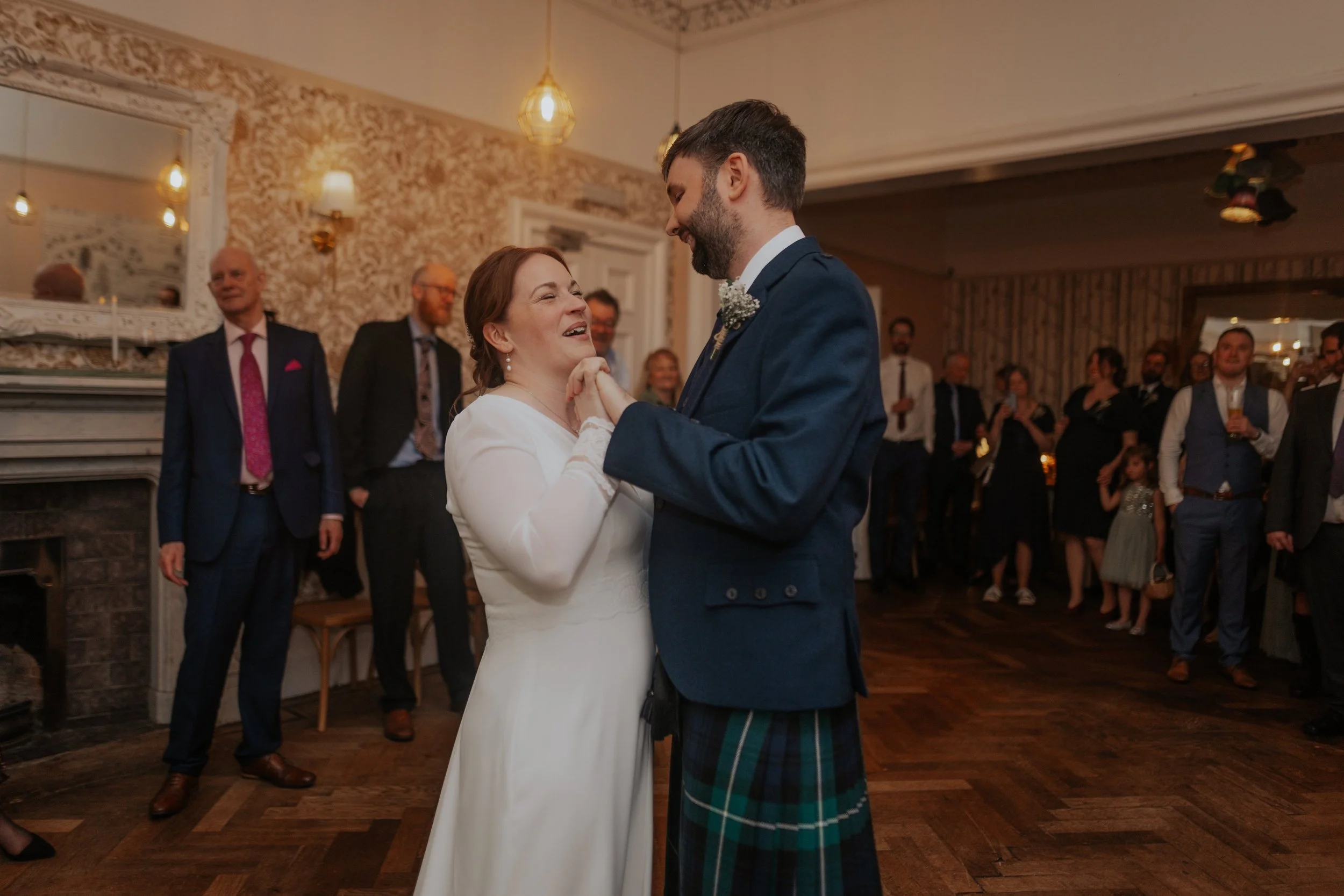 A bride and groom dancing at their wedding reception with guests watching in the background.