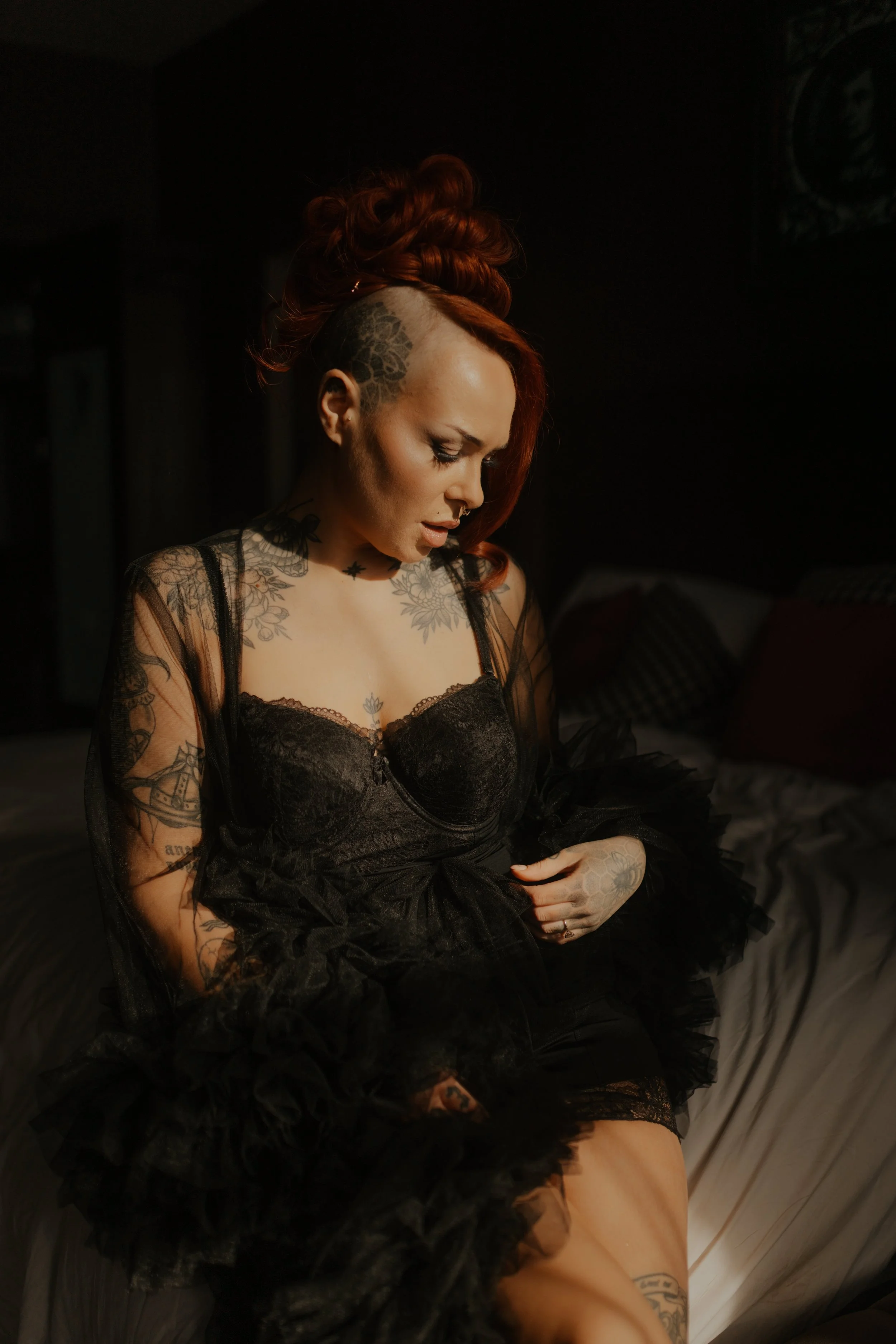 Hana seated in black lace during her wedding preparations, with warm side light on her face and red hair.