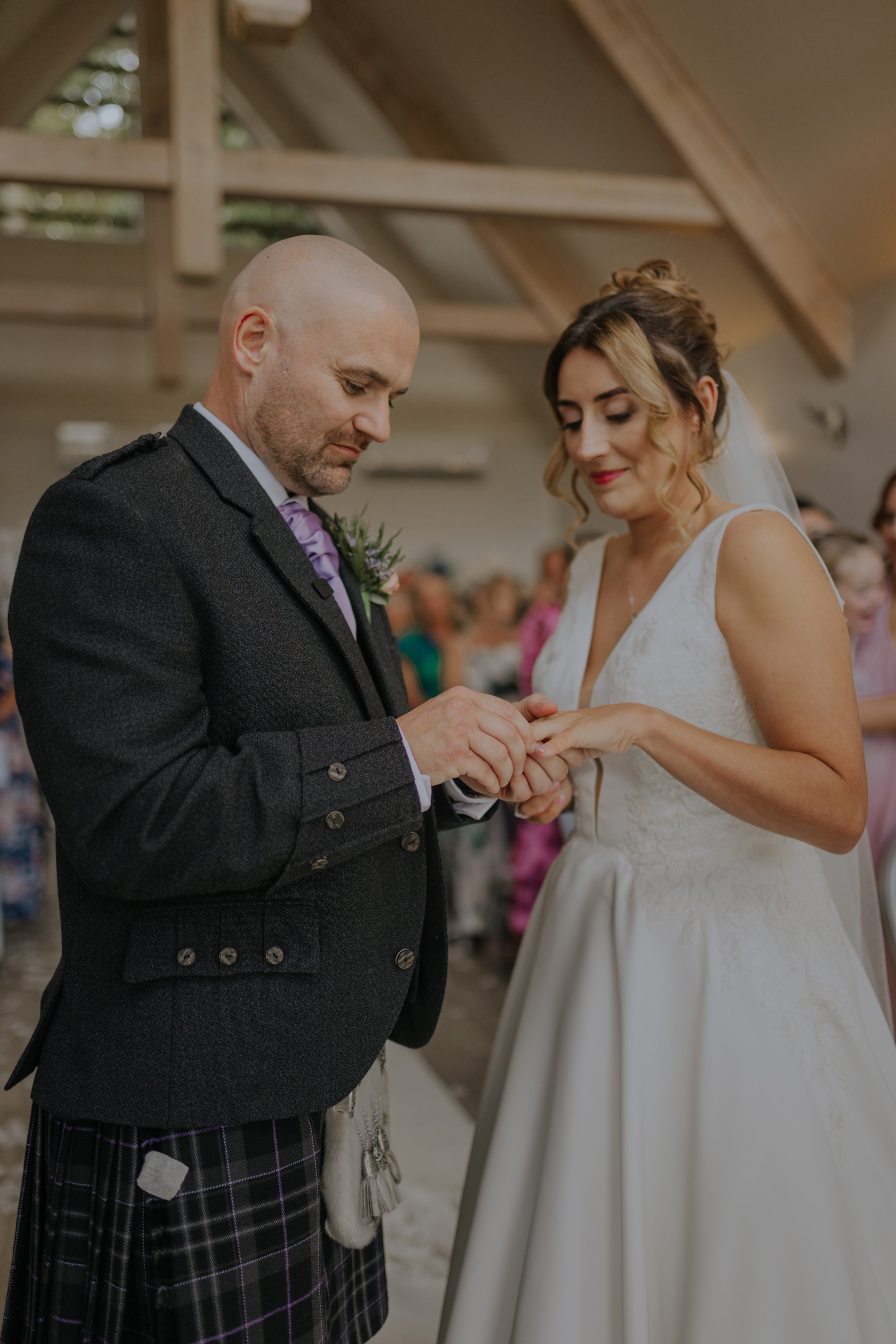 A bride and groom exchanging rings during a wedding ceremony in a rustic wooden venue.