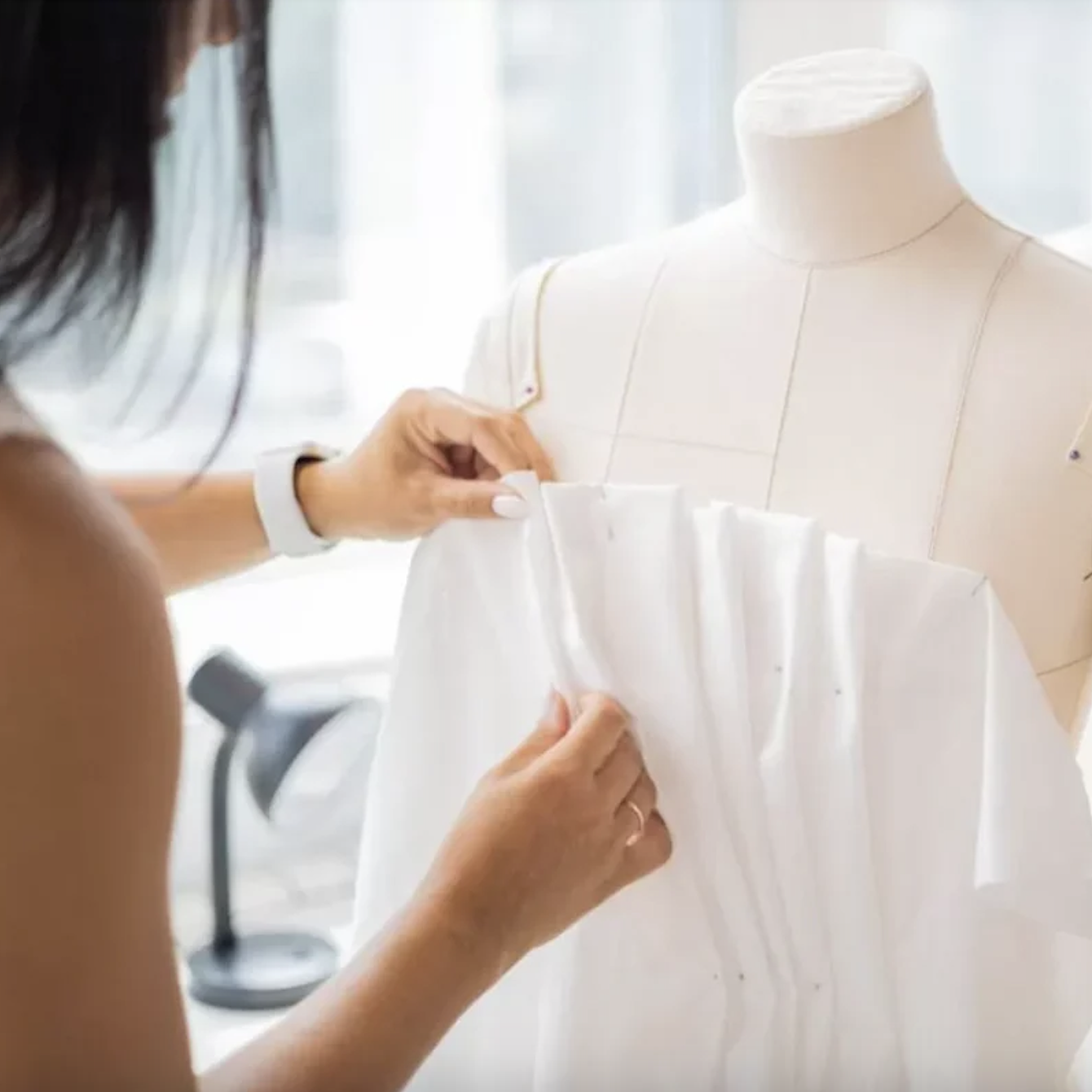 Dressmaker draping fabric on a mannequin during the creation of a handcrafted Caroline Castigliano wedding gown in England.