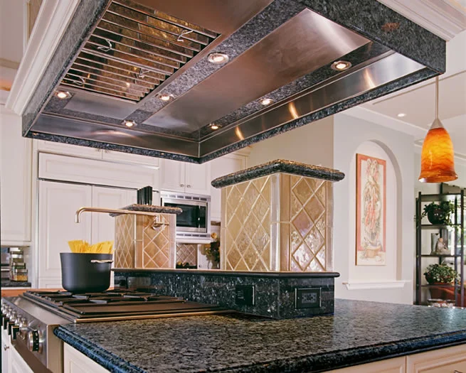 This custom range hood has a stainless steel liner with granite inlay and integrated lighting.
