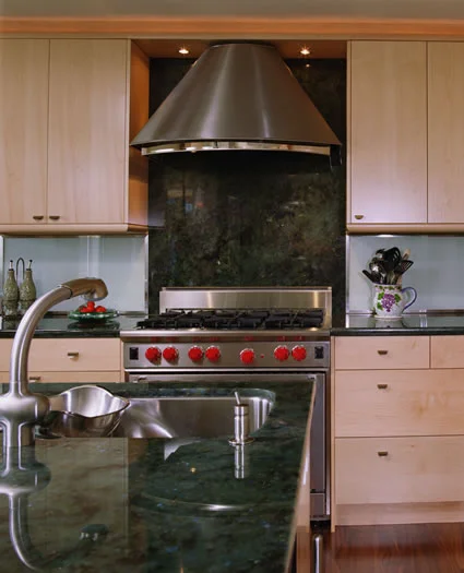 The custom stainless steel hood mounted on the slab granite splash is this kitchens focal point