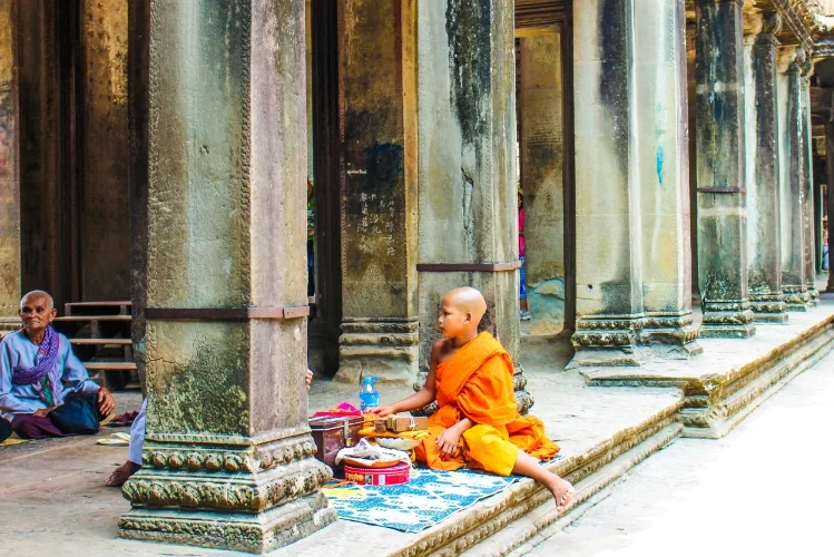 A young monk sits and chants and blesses the visitors of Angkor Wat for donations.