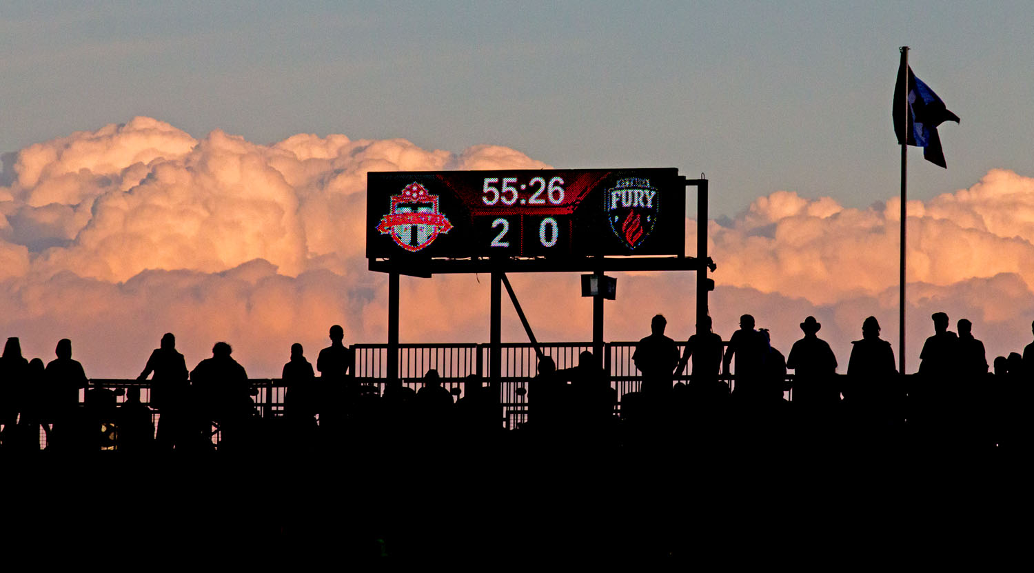 Fans look on during the 56th minute as a the sunset lights up some low lying clouds at the top of BMO Field. Image by Dennis Marciniak of denMAR Media.