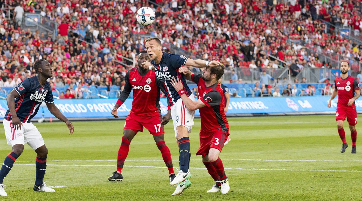 A New England Revolution player heads the ball away from the net at BMO Field. Image by Dennis Marciniak of denMAR
