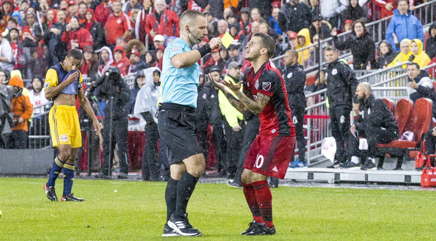 Chris Penso gives Sebastian Giovinco a yellow card in the pouring rain as the match gets out of control. Image by Dennis Marciniak of denMAR Media.