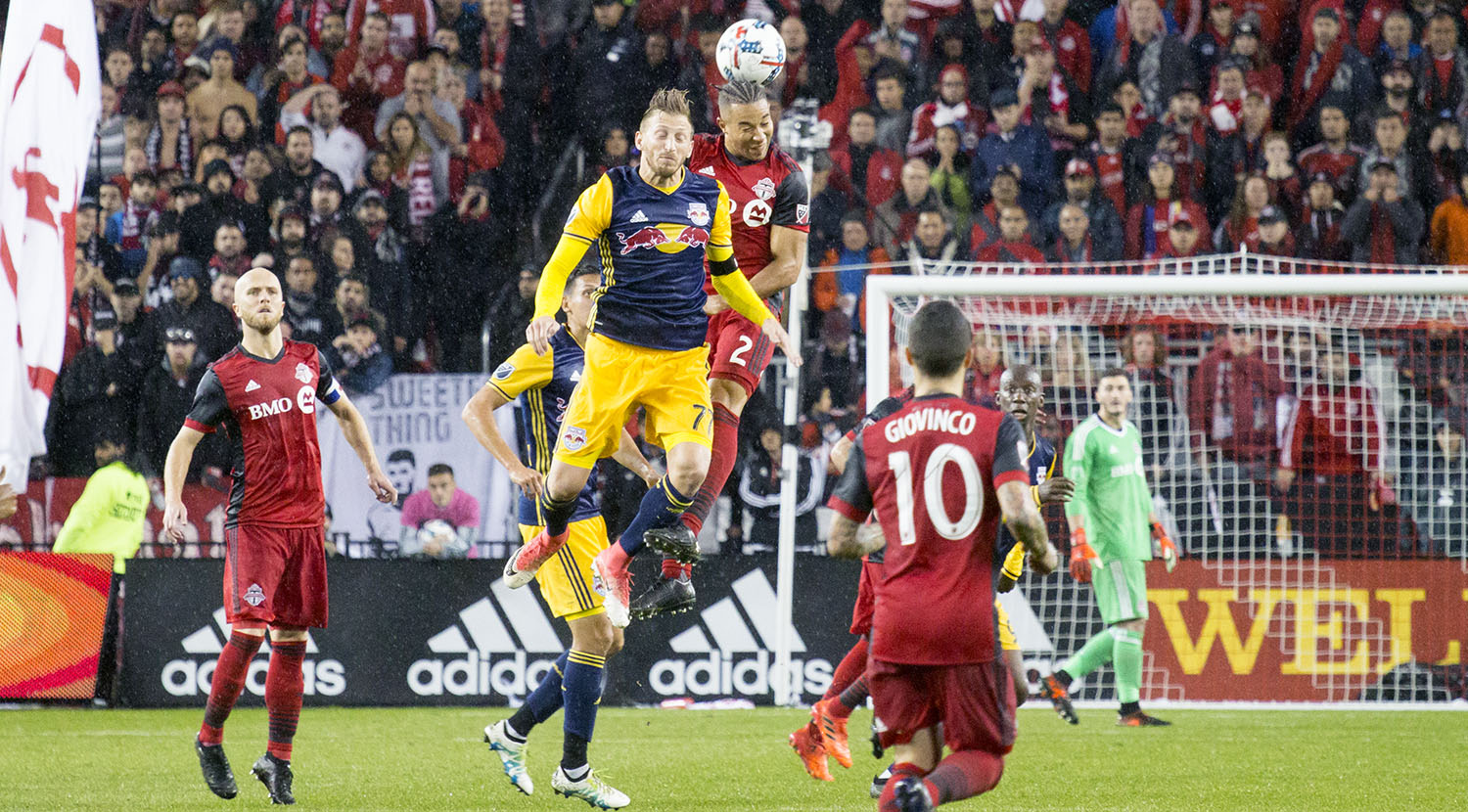 A NYRB and Toronto FC player go into the air for a header during a rainy match in 2017. Image by Dennis Marciniak of denMAR Media.