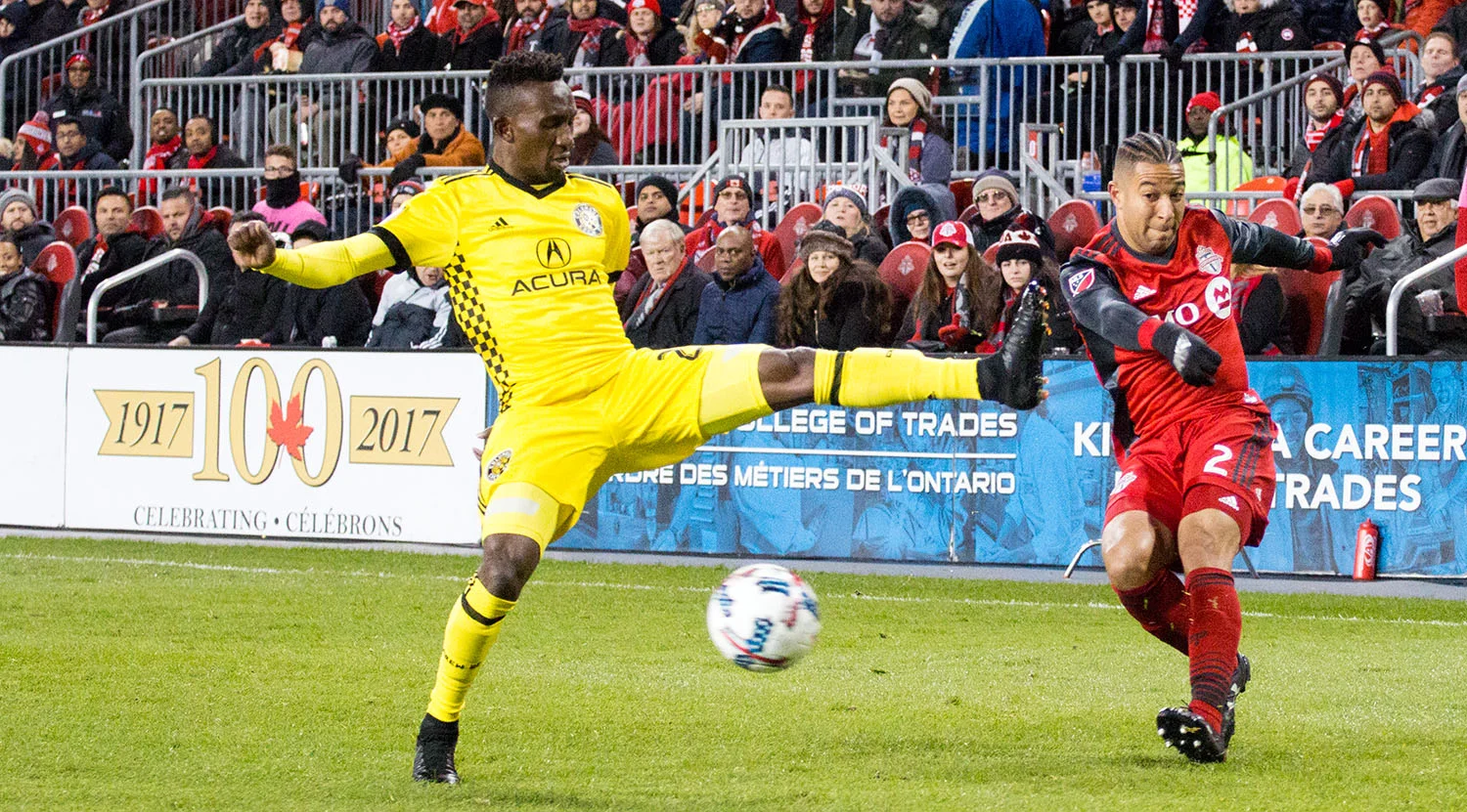 Justin Morrow avoids getting studs penetrating his skin as a Columbus Crew player makes a dangerous attack on the ball. Image by Dennis Marciniak of denMAR Media.
