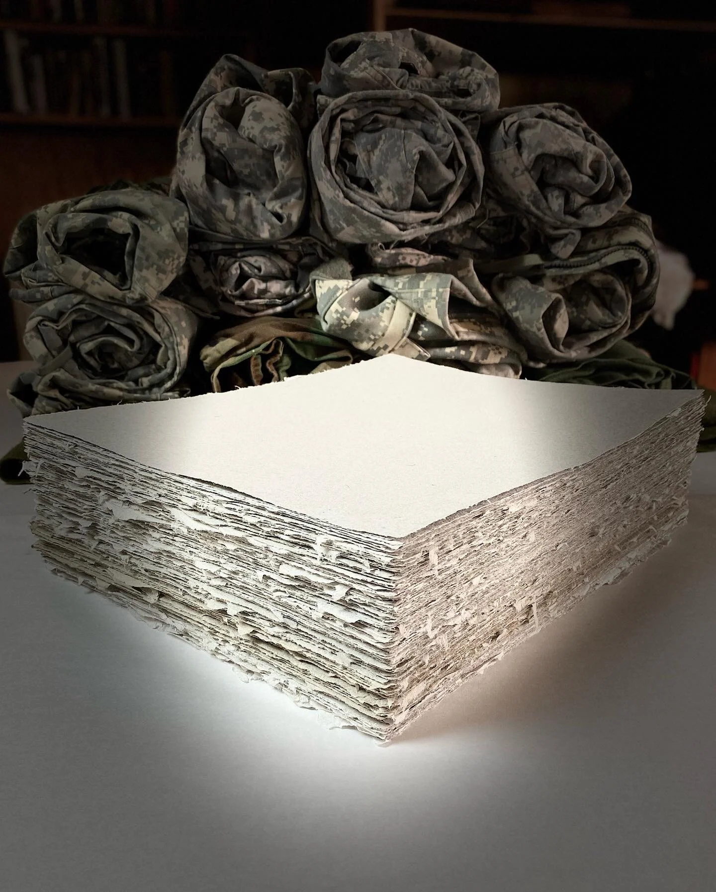 a stack of handmade paper from military uniforms placed in front of rolled up army uniforms