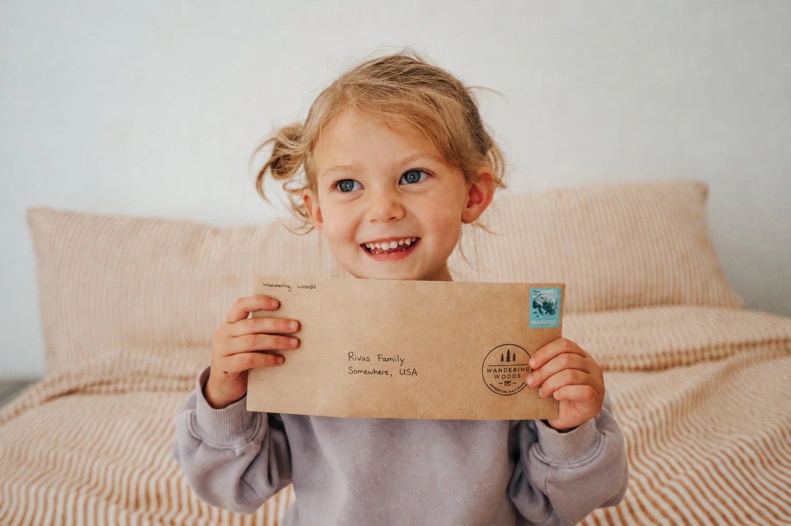A smiling child holding a Wandering Woods Mail Club envelope