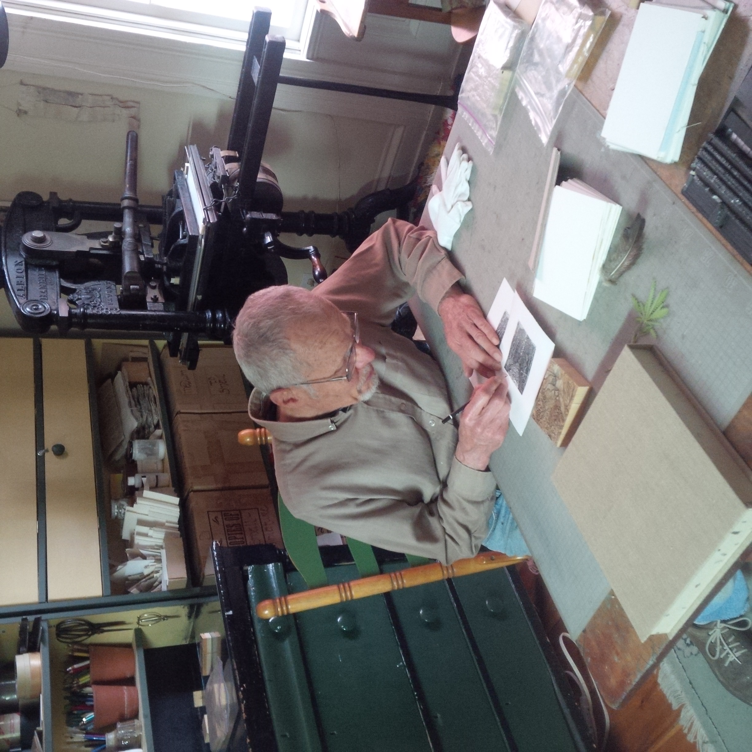 Gerard signing the first print of "Walking Home" at his work table in his heritage home and gallery. His 1882 printing press is behind him.