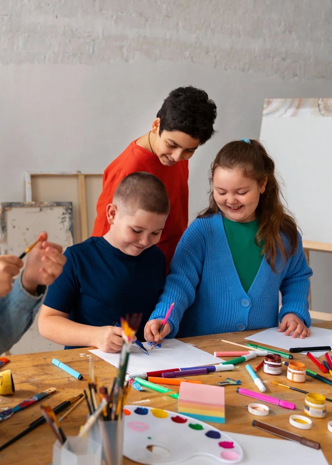 Children engaged in arts and crafts at a table with markers, paints, and paper.