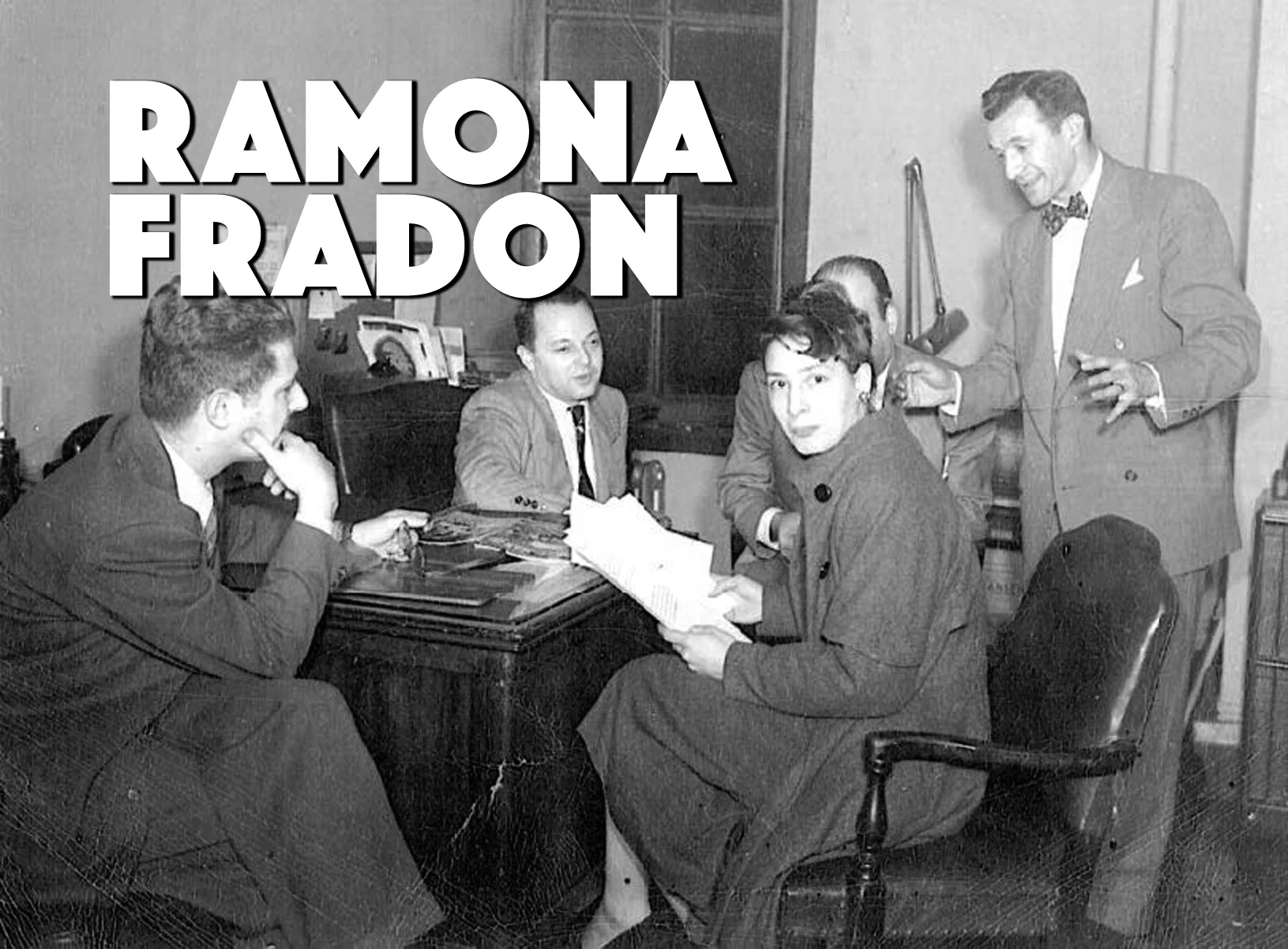Ramona Fradon sitting in a bullpen, surrounded by male co-workers.