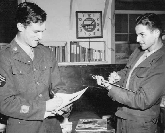 Hugh Hefner (on the left) stands in full military uniform with Hy Eisman sketching (on the right).