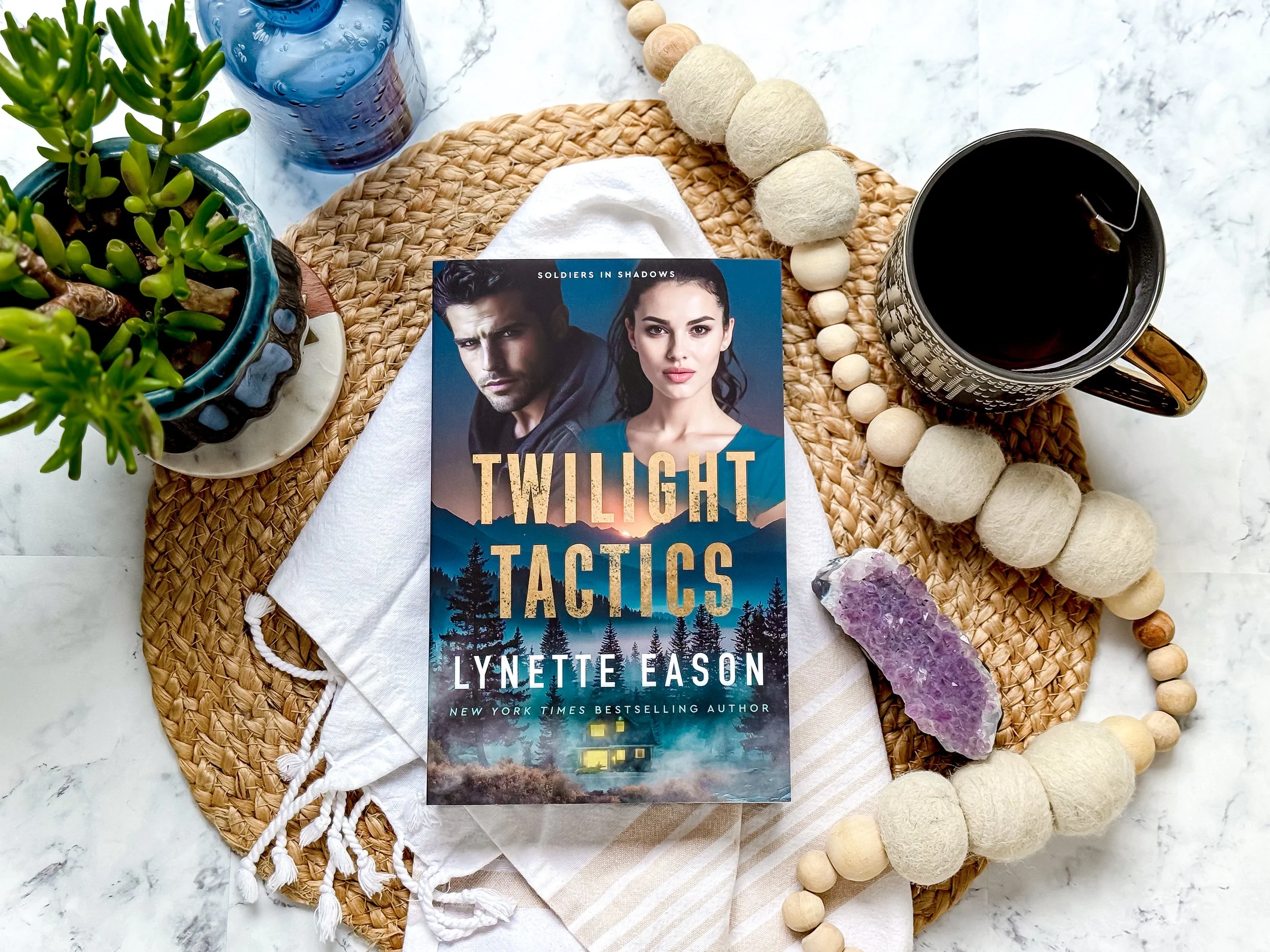 Romantic Suspense Book Mountain Man Woman On Table With Potted Plant, Tea and Purple Gemstone