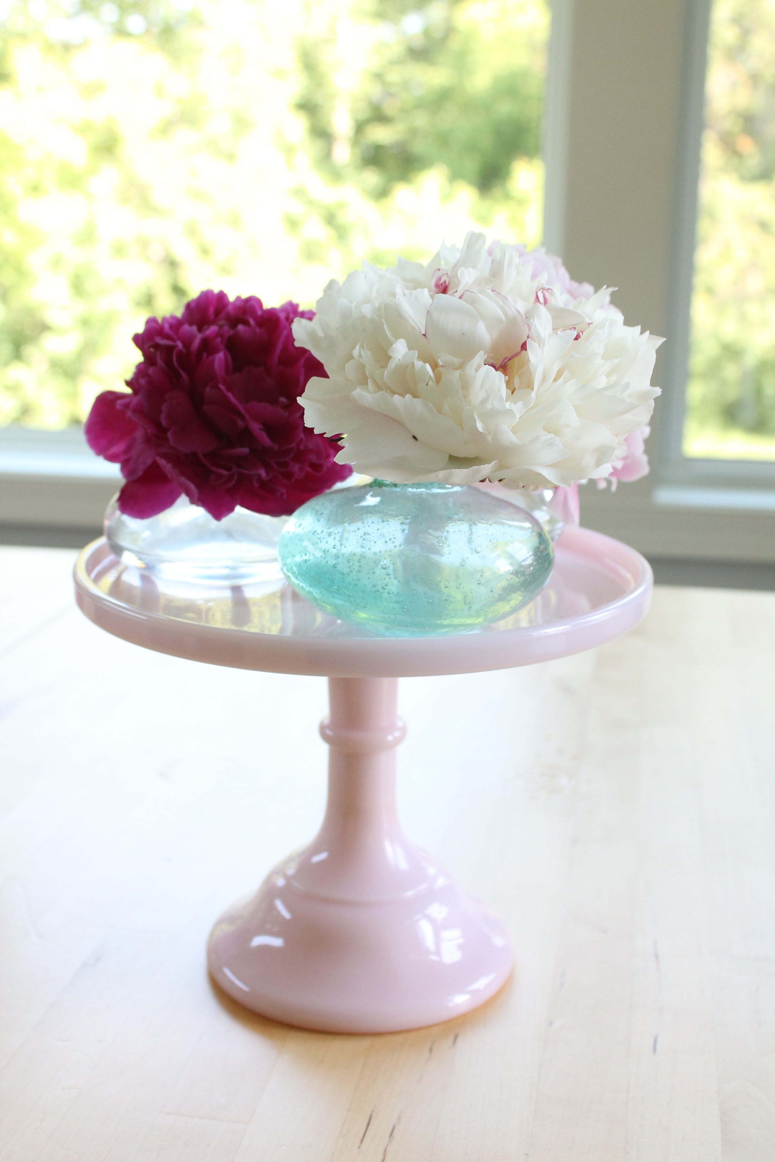Peonies in bud vases on a pink cake plate.
