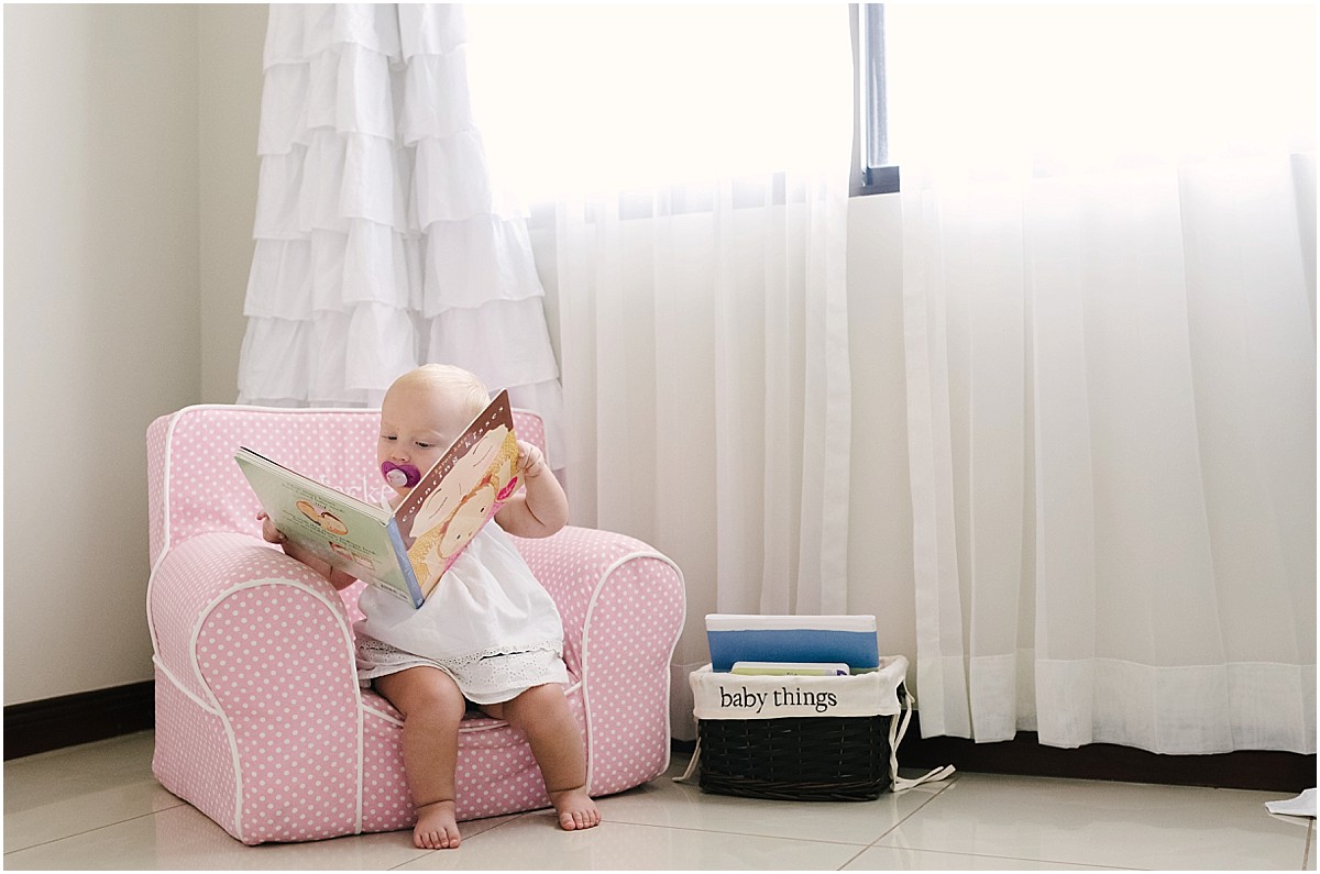 one year old baby girl reading in a chair