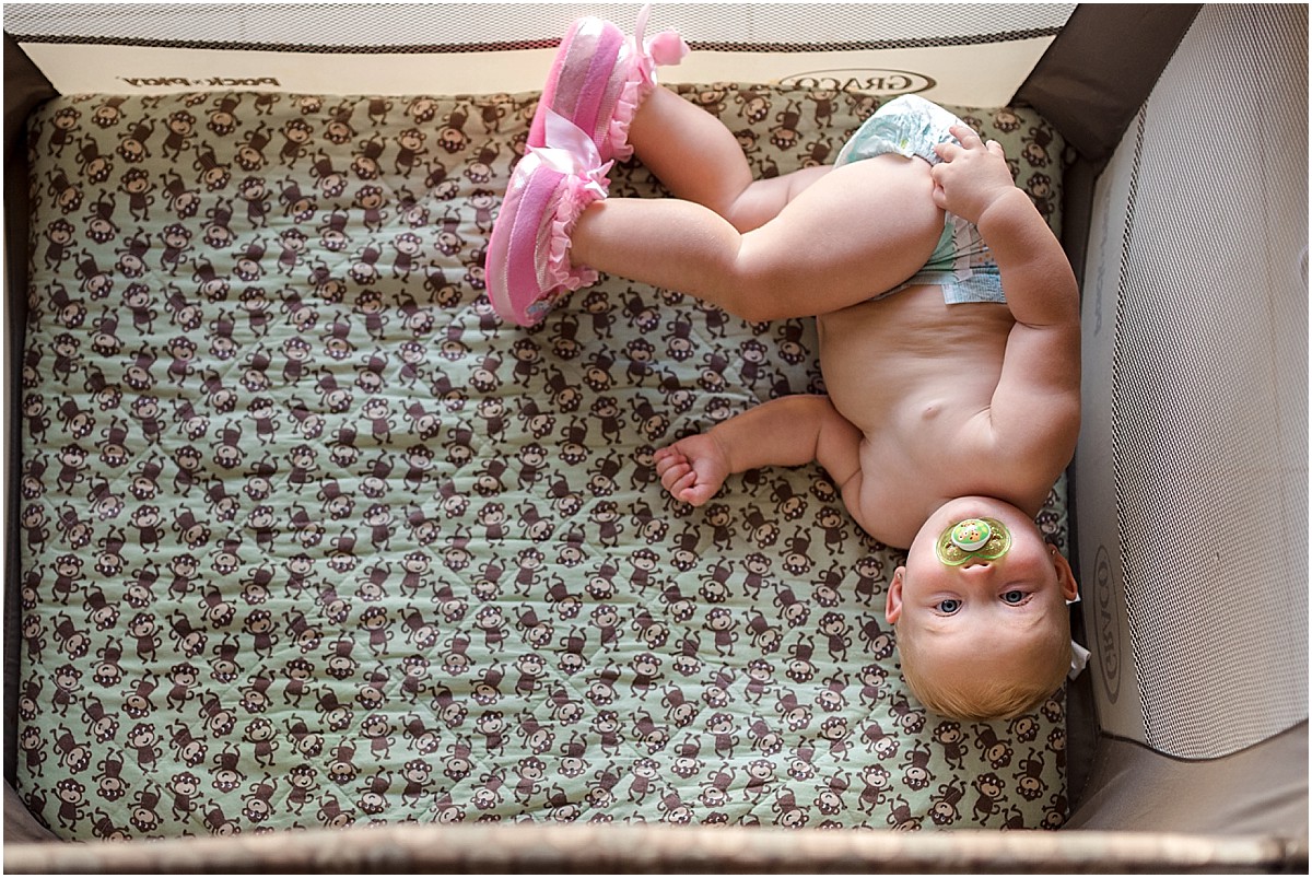one year old baby in playpen with diaper and pink slippers
