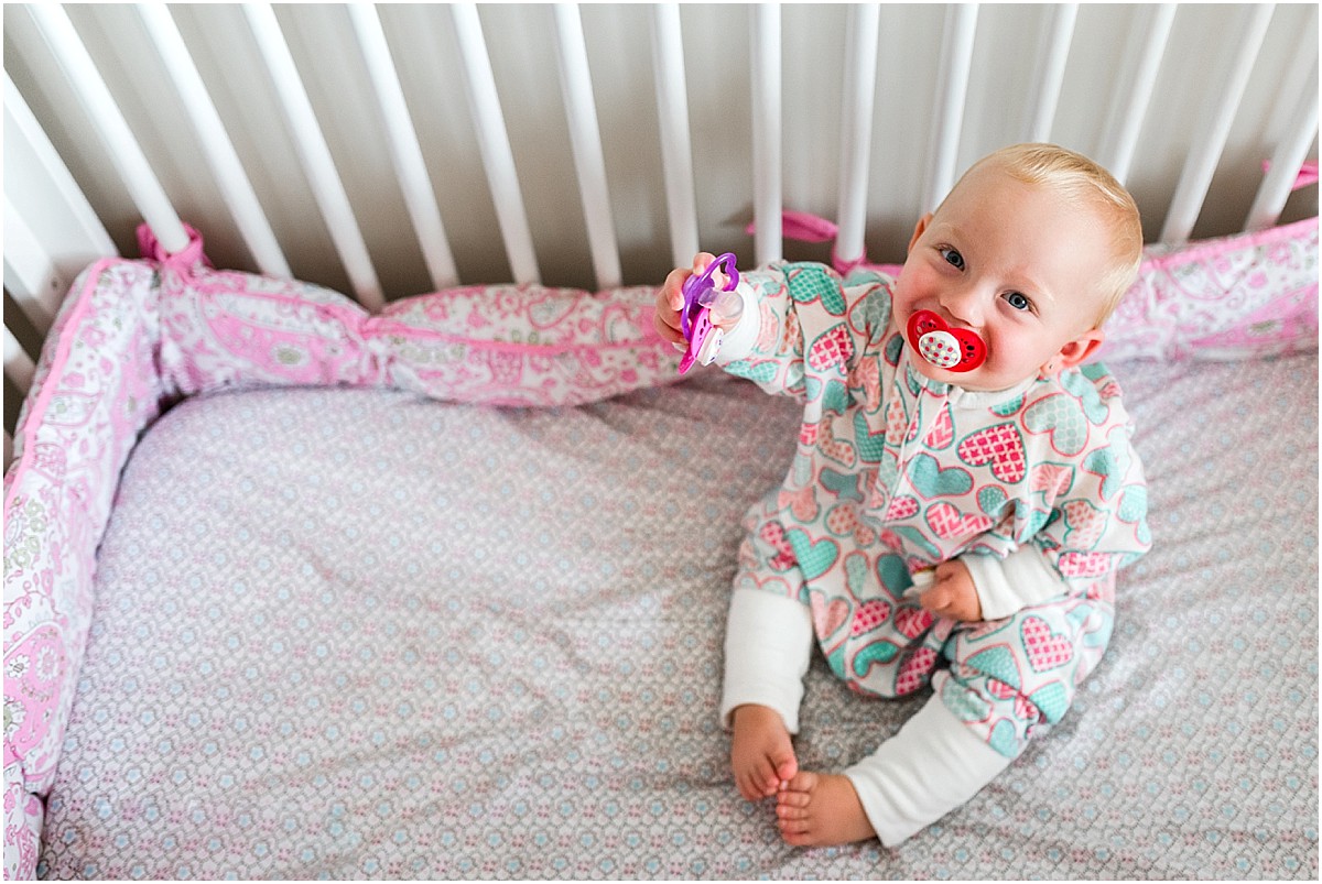 Baby girl in zipadee zip sleep sack with pacifiers in crib