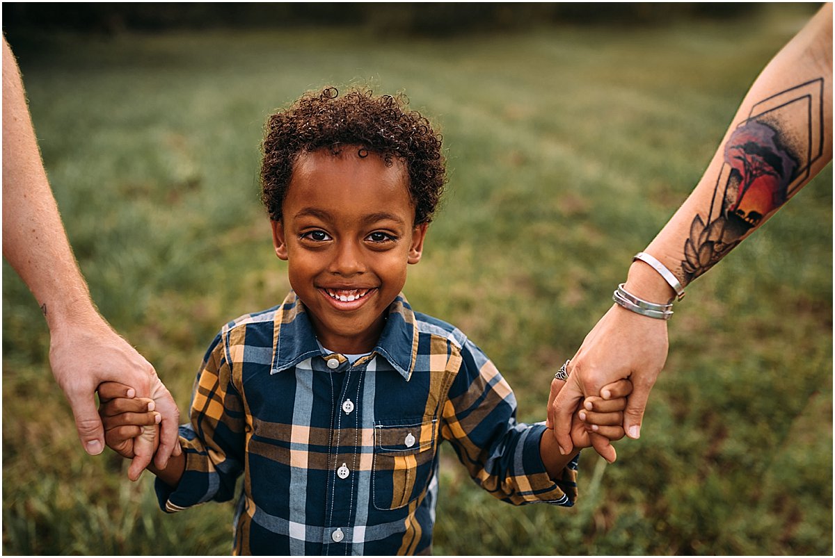 Little boy adopted from Ethiopia holding mom and dad's hand with meaningful tattoo.