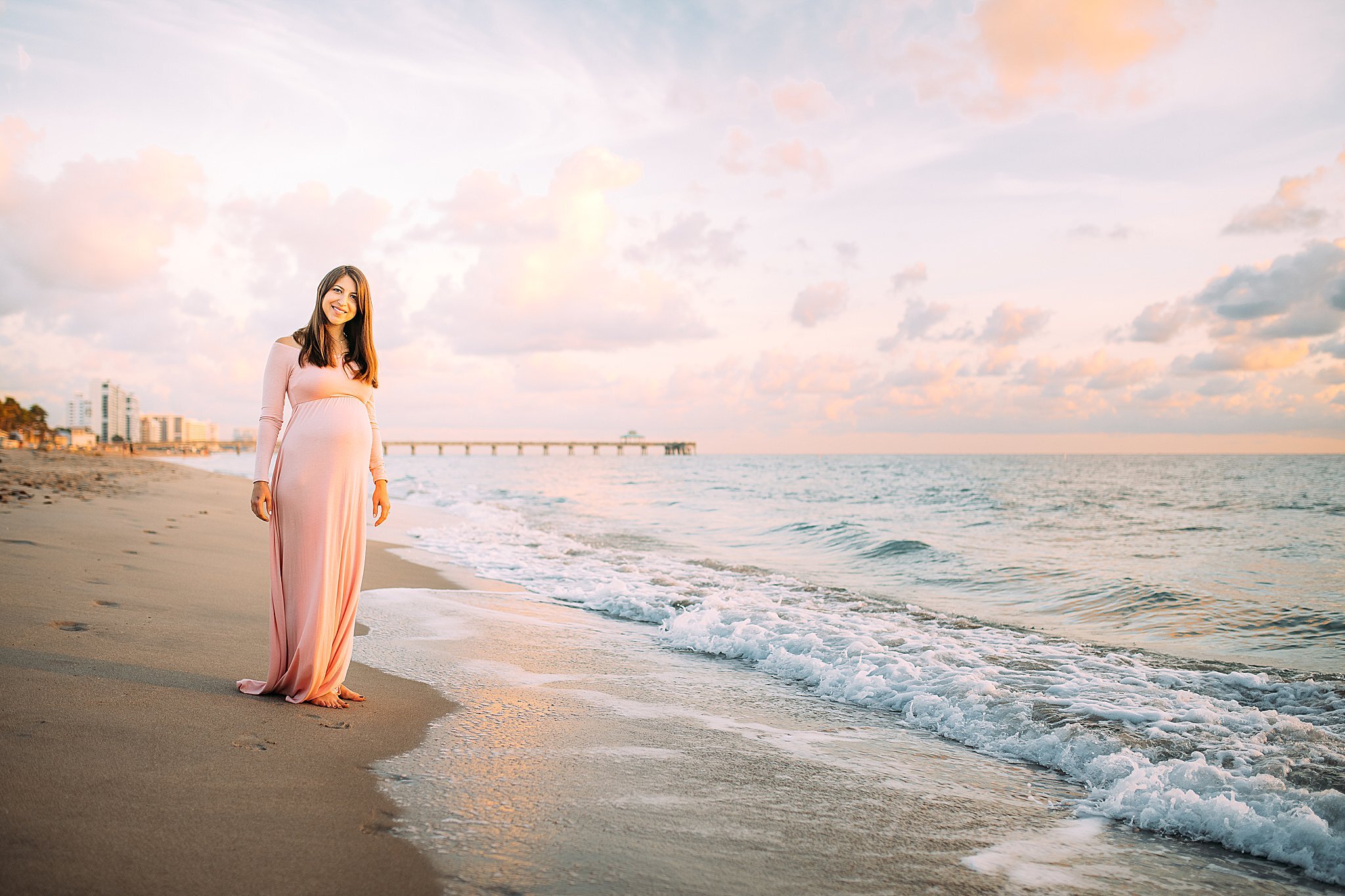 Expecting mother on the beach at sunrise showcasing beautiful pregnant belly.