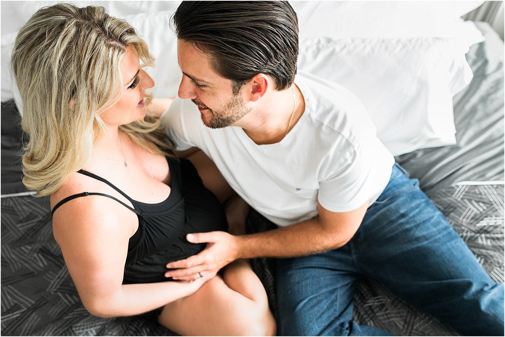 Couple laying on their bed touching pregnant belly during in-home maternity session in Orlando Florida.