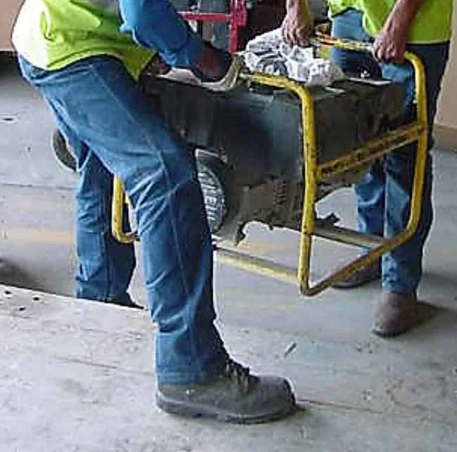Workers lifting a heavy generator while wearing steel-toed work boots.
