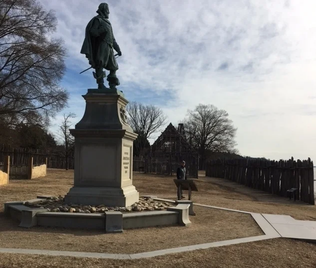Dr. John F. Chappo at Historic Jamestowne in December 2016 standing within the reconstructed James Fort walls and next to the statue of Captain John Smith.