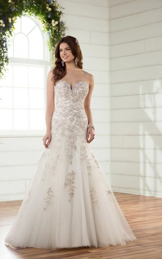 D2398 - Made for the bride who wants to be a princess on her big day, this sparkling, A-line designer wedding dress by Essense of Australia is magical! Lace and tulle form a sweetheart neckline and frothy skirt, which is richly beaded around the bodice. The beadwork continues down the length of the full skirt and into the long, sweeping princess train. Silver lace plays up the metallic finish and dropped waist. The back of this shimmering princess gown is available in a lace up back, or as an easy close zipper under classic crystal buttons. Also available in plus size, this princess dream dress is perfect for any “I Do.” Colors Available - White/Silver, Ivory/Silver