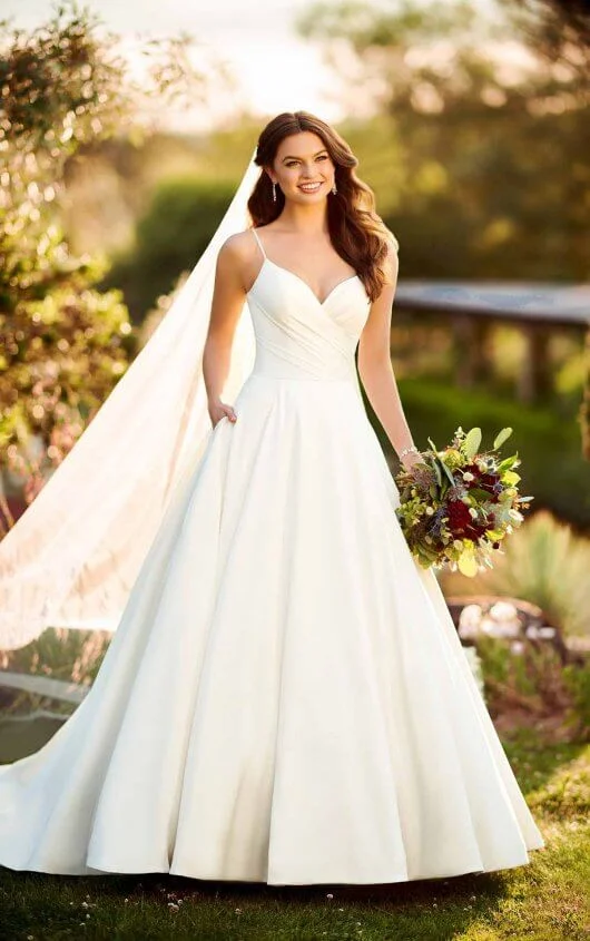 D2753 - A casual take on the classic ballgown silhouette, this relaxed ballgown with scoop back from Essense of Australia was designed with the no-fuss bride in mind. Soft ruching highlights the bodice of this gown, accented with a slight V-neckline and shoestring straps. From the waist, the Mikado fabric extends into a ballgown skirt, complete with pockets. Available in - White, Ivory
