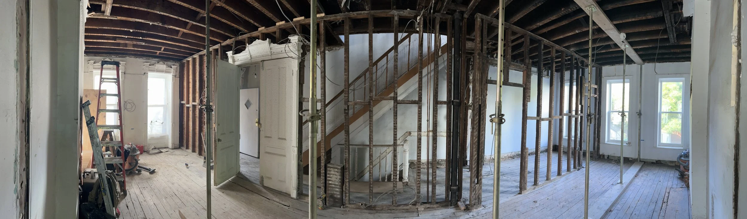 Interior of a house under renovation with exposed wooden beams, construction tools, scaffolding, and unfinished walls.