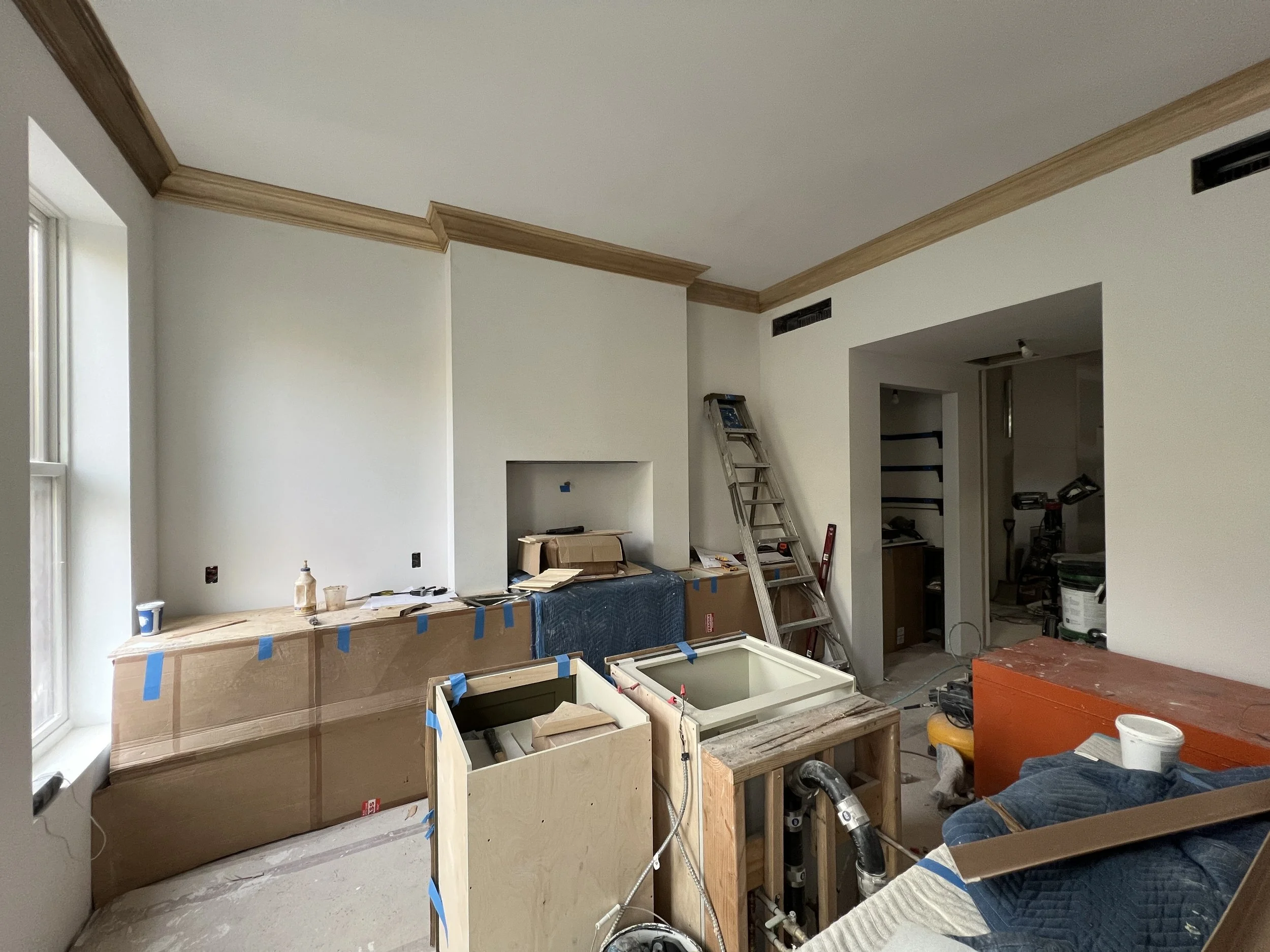 Interior of a room under renovation with partially installed crown molding, construction materials, and tools scattered around.