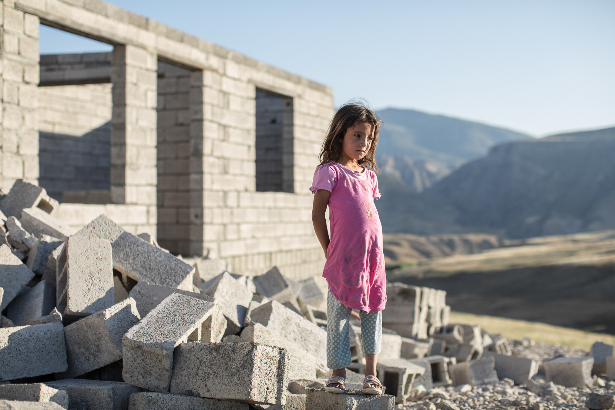  Yazidi girl stands atop craggy blocks at a neighboring camp under construction for newly arrived Syrians in the area (2017). 