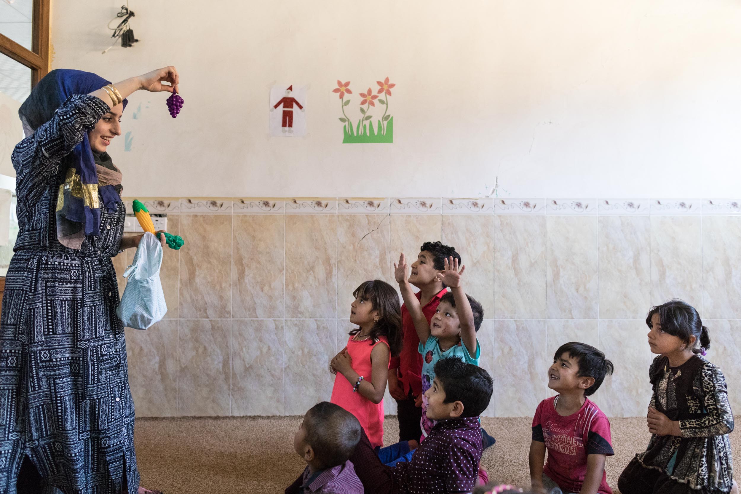  Teacher at the local school for the displaced holds plastic grapes as the children name the fruit or vegetable (2016). 