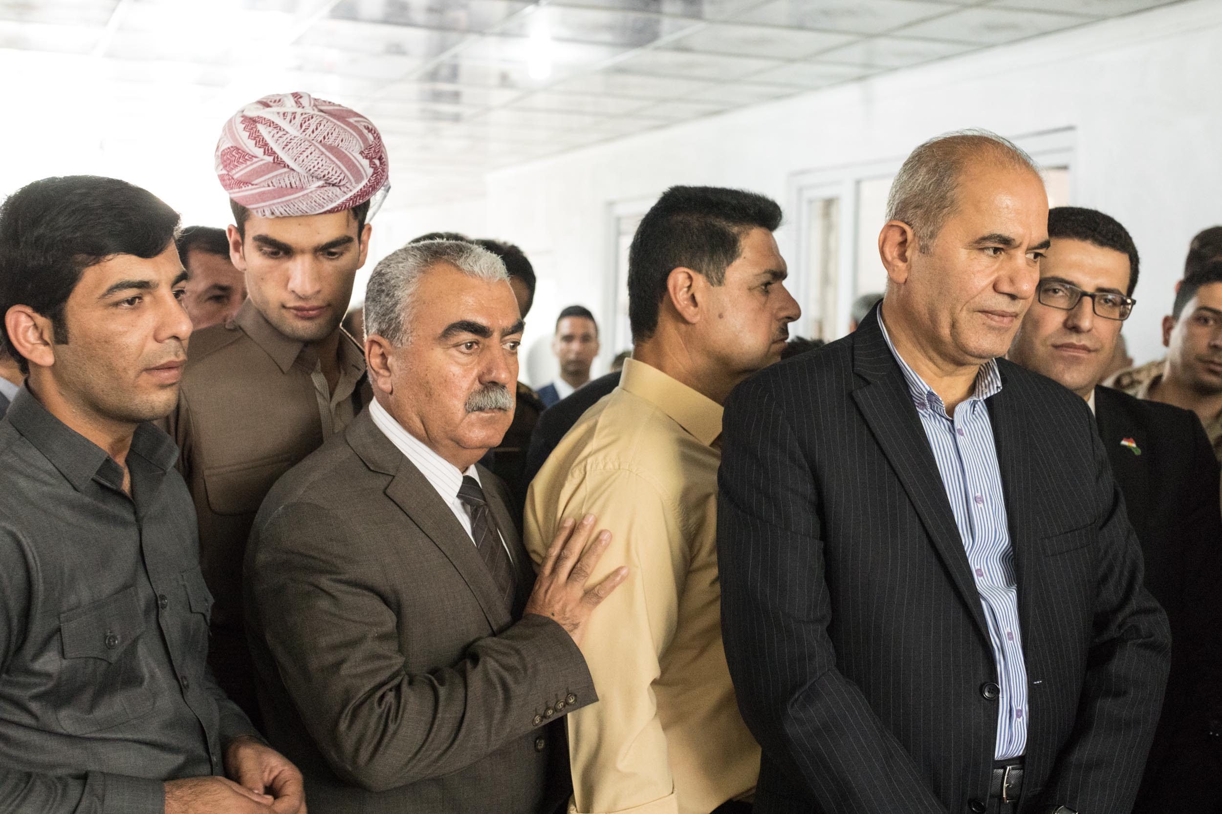  Men crowd around a desk to watch the mayor of the town sign documents commemorating the efforts of deceased Peshmerga fighters (2017). 