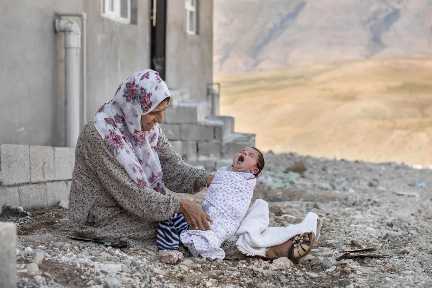 Syrian woman holds her grandchild outside her home at a refugee camp in Azadi, Iraq (September 2017). 