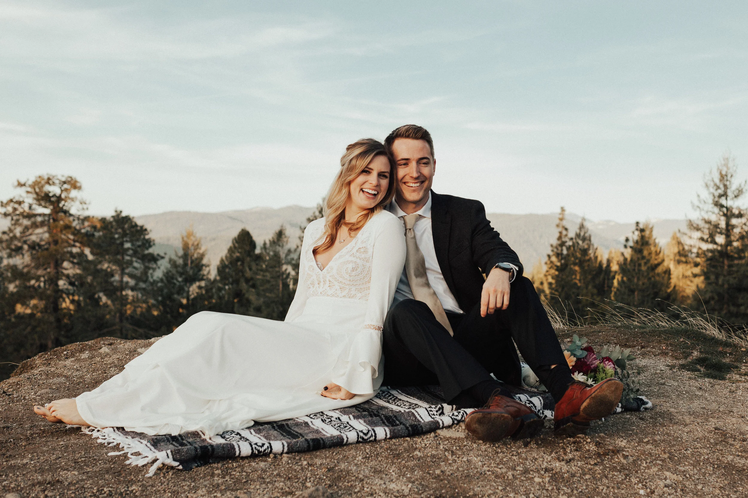 Bride and groom sitting snuggled up on a blanket after just getting married on the cliff side in nevada city, california.
