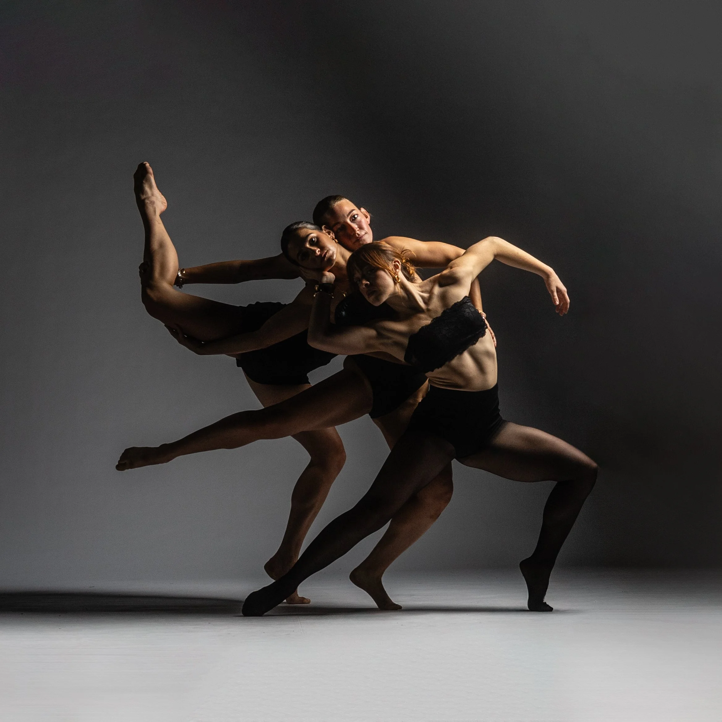 A group of dancers forming a human pyramid pose against a dark background.